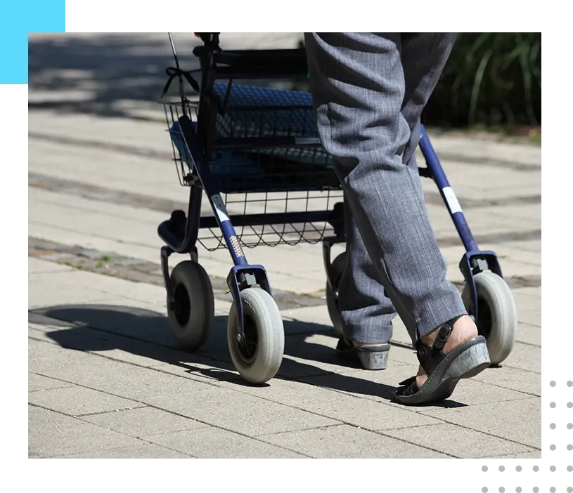 A person with blue jeans and sandals is pushing a walker.